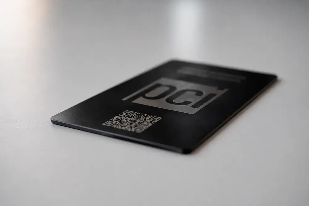 A black metal Bümpis card lying at an angle in low light, its etched logo catching the light